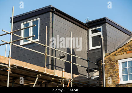 Scaffolding to a newly completed dormer / dormers / dormas / dorm roof extension with slate tile cladding on the roof on a Victorian terraced house in Twickenham. London. UK Stock Photo