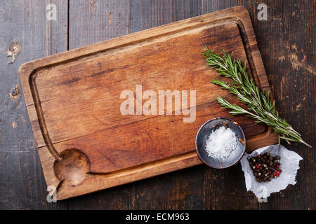 Chopping board, seasonings and rosemary on dark wooden background Stock Photo