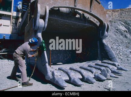 A welder repairs a giant shovel bucket in an open pit mine. Stock Photo