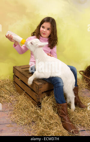 Lovely girl feeding a newborn baby goat with a milk bottle Stock Photo