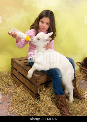 Lovely girl feeding a newborn baby goat with a milk bottle Stock Photo