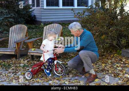 Grandfather teaching his Granddaughter to ride a tricycle Stock Photo