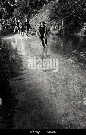 A woman runs along a flooded footpath whilst three people look on laughing as she splashes through the water Stock Photo