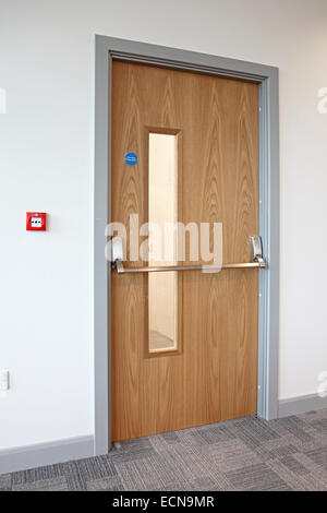 Oak finished fire escape door in a modern office. Shows panic bar, fire door sign and wall-mounted fire alarm button Stock Photo