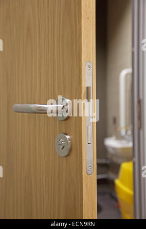 A partially open, modern, oak-finish interior door showing door handle, lock and mechanism and disabled toilet beyond Stock Photo