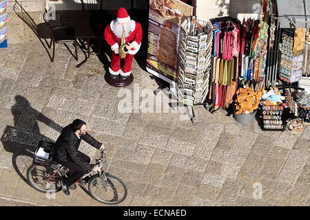 A religious Jewish man rides a bicycle past a Santa Claus figure near the Jaffa Gate as viewed from the Herodian Phasael Tower atop the Jerusalem Citadel, known as the tower of David. The 'Kishle' and the citadel moat at the Tower of David Museum of Jerusalem History have just recently been opened to the public allowing exploration of new archaeological findings shedding light on layers of the city's history dating back to the First Temple era in the 8th century BCE. Stock Photo