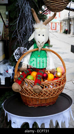 Toy goat in a green jacket sits on a basket with toys Stock Photo