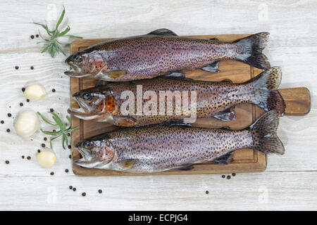 Top view of fresh trout being prepared, skin coated with oil, for cooking on server board. Herbs and spices on white aged wooden Stock Photo