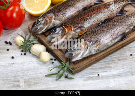 Close up of fresh wild trout being prepared, skin coated with oil, for cooking on server board. Herbs, tomatoes, lemon and spice Stock Photo