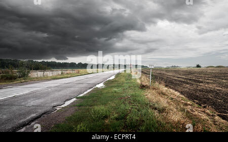 Road in cloudy weather against thunderclouds Stock Photo