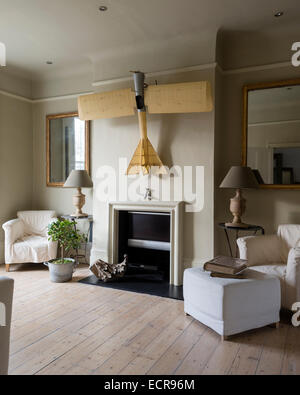 Large scale model airplane hung above fireplace in spacious living room with wooden flooring, armchairs and gilt framed mirrors Stock Photo