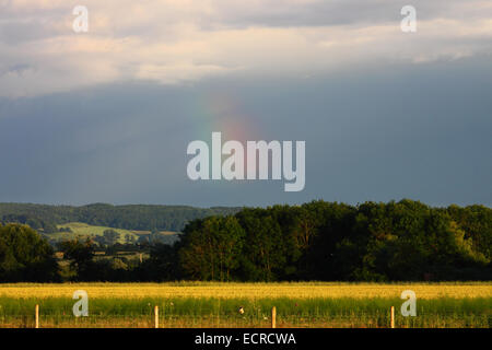 A part of a rainbow above fields on the horizon with dark clouds above. Stock Photo