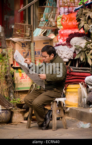 A man in Xi'an, China, sits reading his morning paper beside his stall Stock Photo