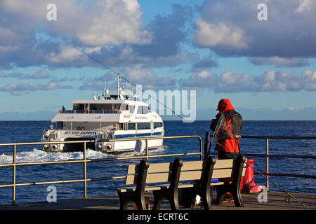 Man Fishing Off The Jetty On The Cabrillo Mole In Avalon, Catalina Island, California, The Departing Catalina Express SeaCat Ferry In Background. Stock Photo