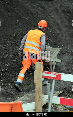 Worker wearing orange uniform pushing wheelbarrow on the construction site Stock Photo