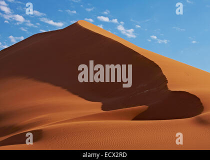 View of sand dunes in desert with blue sky and clouds in background