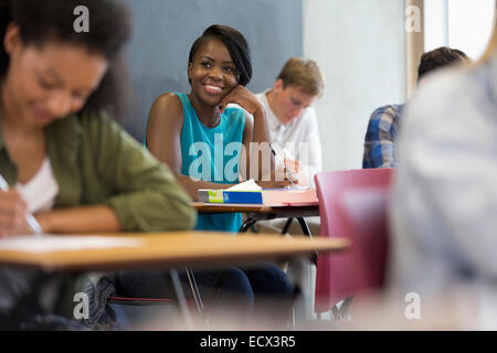 Smiling university student sitting at desk with hand on chin Stock Photo