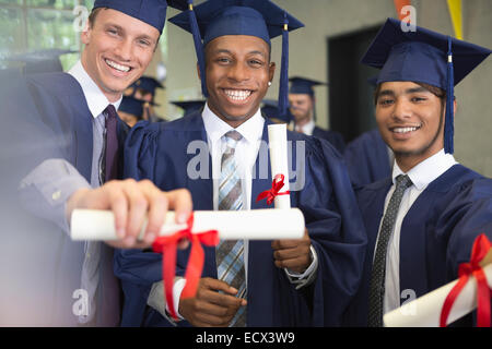 Portrait of smiling university students holding diplomas after graduation ceremony Stock Photo