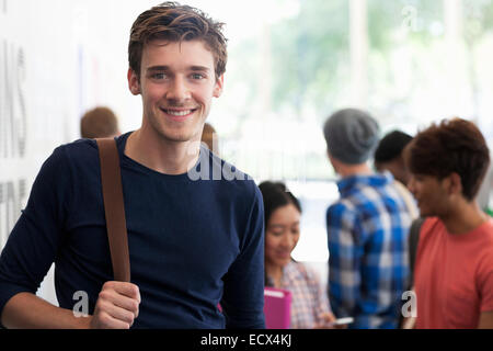 Portrait of smiling university student standing in corridor during break, people in background talking Stock Photo