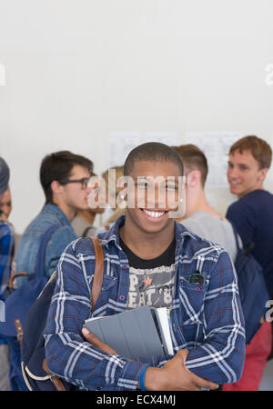 Male student holding books and smiling at camera with other students in background Stock Photo