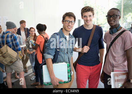 Three smiling male students standing together with other students in background Stock Photo