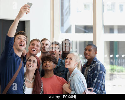 Group of laughing students taking selfie on corridor with large window in background Stock Photo