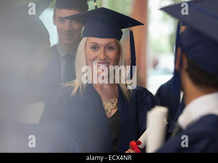 Female student smiling in graduation clothes surrounded by other students Stock Photo