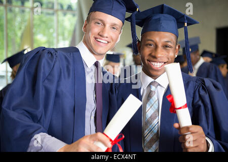 Two laughing male students in graduation clothes holding diplomas Stock Photo