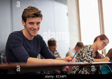 Male student smiling at camera and sitting at desk during lecture Stock Photo