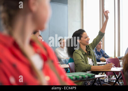 Female student raising hand during lecture with other students in background Stock Photo