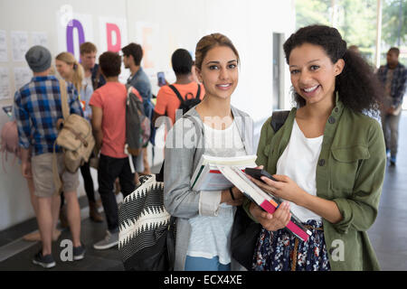 Portrait of two smiling female students holding books, other students in background Stock Photo