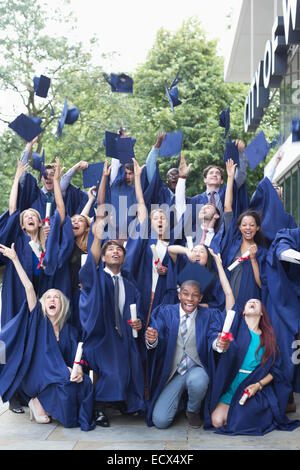 Group portrait of students in graduation gowns throwing mortarboards in the air Stock Photo