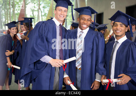 Portrait of three smiling male students in graduation gowns holding diplomas Stock Photo