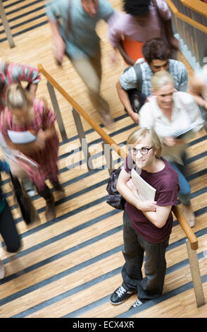 Portrait of young male students holding notes standing on stairs with other students going up Stock Photo