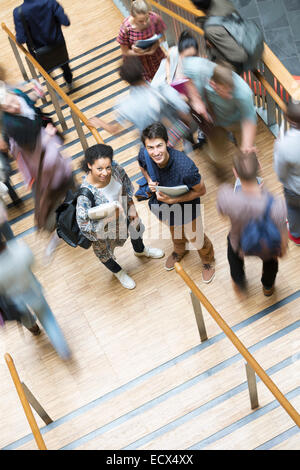 Elevated view of two smiling students standing on stairs with other students going up and down Stock Photo