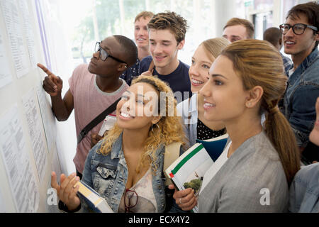 Group of smiling students holding books and looking at information board Stock Photo