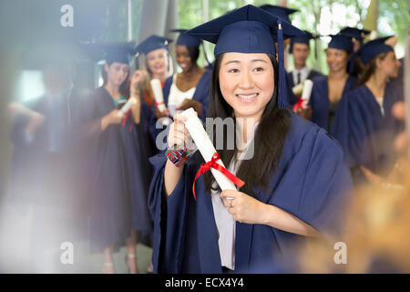 Portrait of smiling female student in graduation gown holding diploma Stock Photo