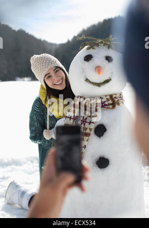 Man photographing woman with snowman Stock Photo