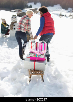 Couple pulling sled with Christmas gifts in snow Stock Photo
