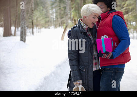 Man surprising woman with gift in snow Stock Photo
