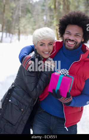 Portrait of couple with Christmas gift hugging in snow Stock Photo