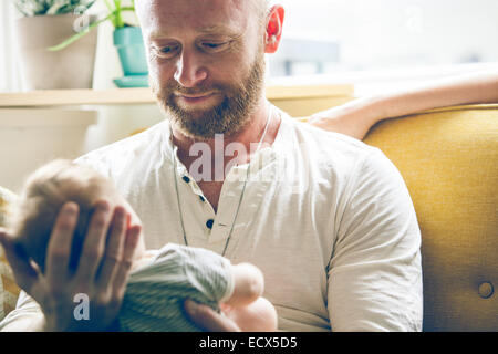 Portrait of father holding baby, sitting on sofa beside mother Stock Photo