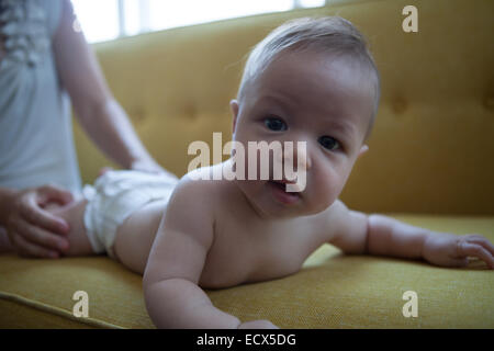 Portrait of little baby lying on front on yellow sofa, looking at camera Stock Photo