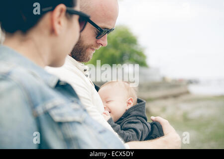 Parents wearing sunglasses holding little baby outdoors Stock Photo