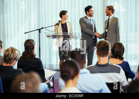 Businessmen shaking hands during presentation in conference room, businesswoman smiling Stock Photo