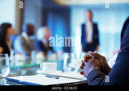 Businessman sitting at conference table in conference room with hands clasped Stock Photo