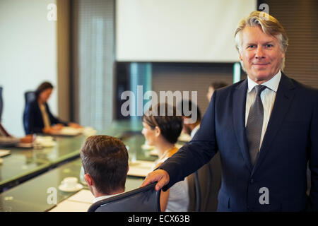 Portrait of businessman standing in conference room with colleagues in background Stock Photo