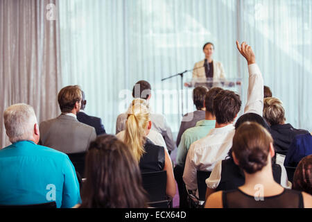 Businesswoman giving presentation in conference room, people raising hands Stock Photo