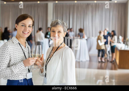 Two businesswomen standing with champagne flutes in hands, colleagues in background Stock Photo
