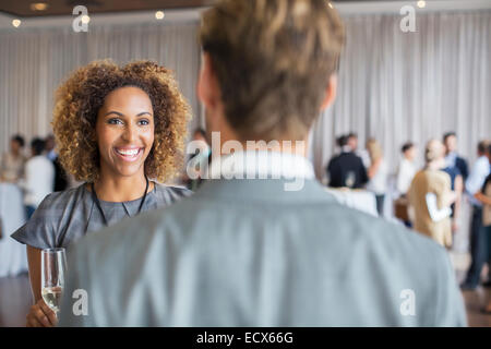 Two business people standing with champagne flutes, smiling and talking in conference room Stock Photo